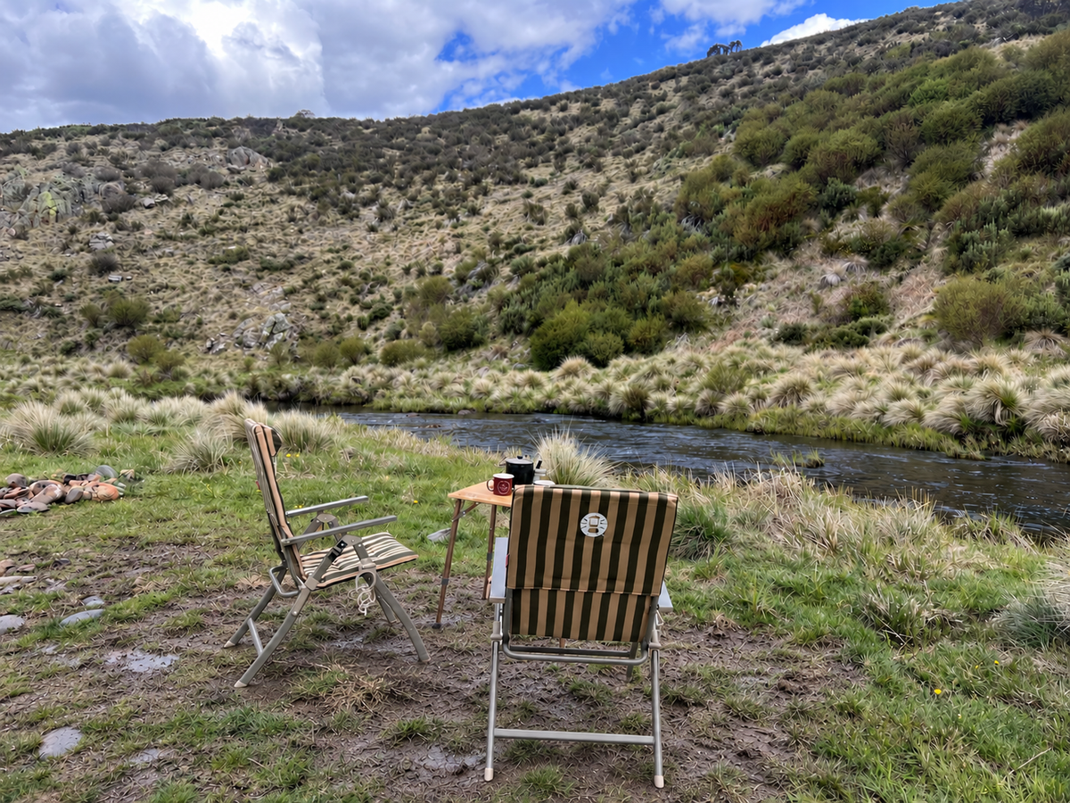 A muddy campsite by the river with two chairs and a table